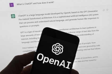 The OpenAI logo is seen on a mobile phone in front of a computer screen which displays output from ChatGPT, Tuesday, March 21, 2023, in Boston. (AP Photo/Michael Dwyer)